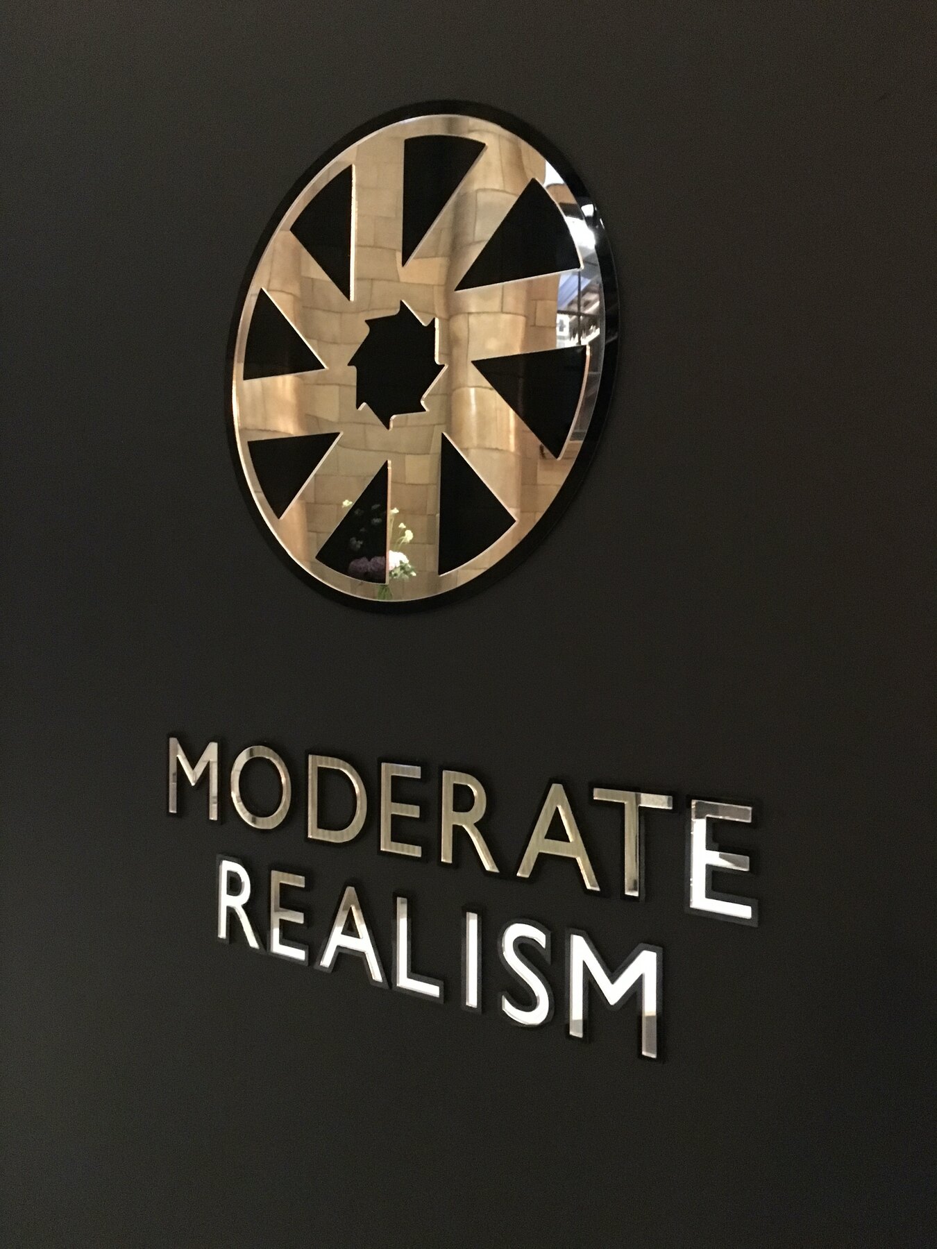 Black and gold Moderate Realism plaque beside the mirrored installation