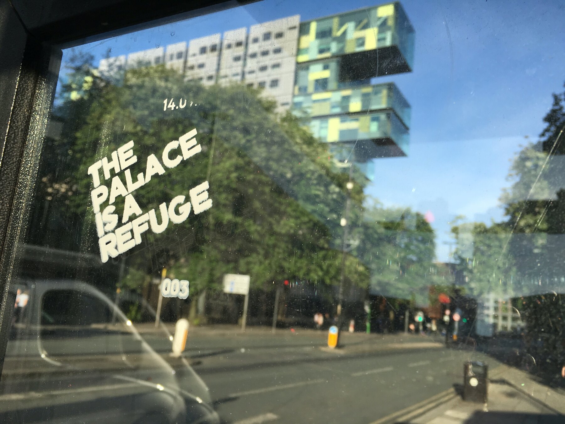 The Palace Is a Refuge printed in white ink on bus shelter glass in Manchester