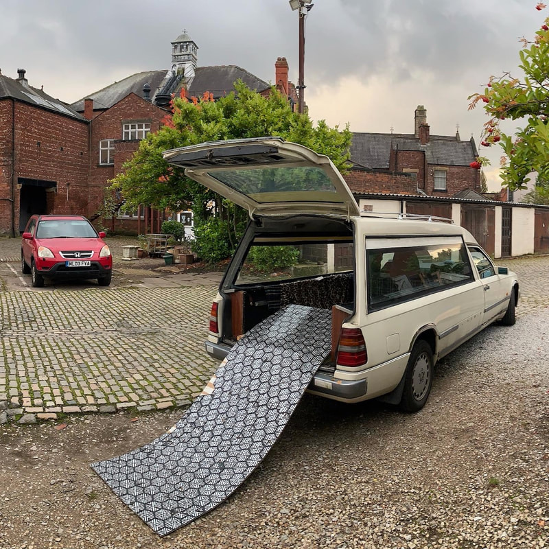 Martha the hearse with her tailgate up and a printed mat rolled out, Manchester