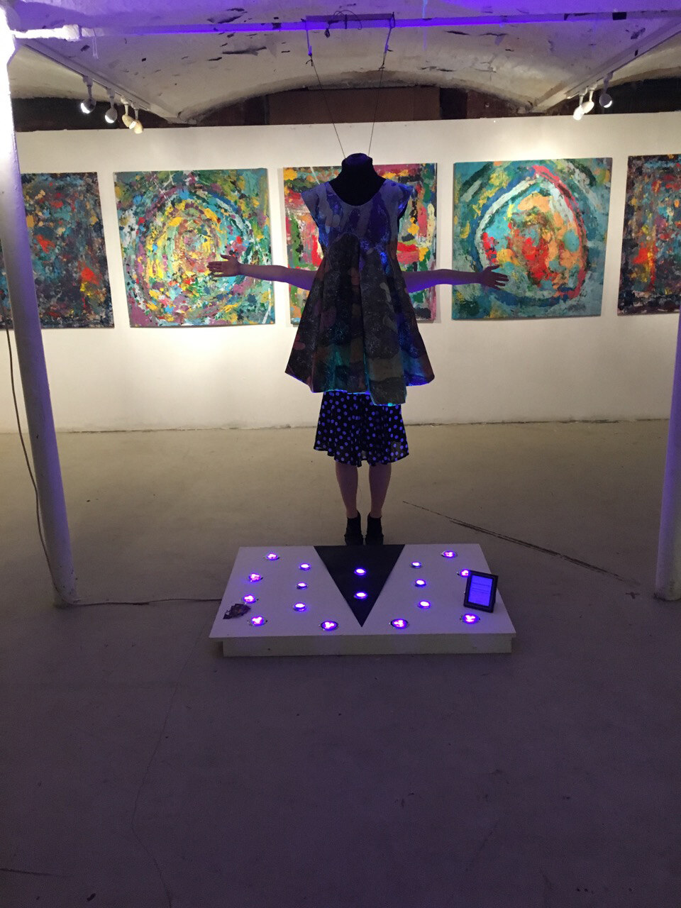 A dress by the artist Sally Gilford, displayed on a headless mannequin above a lit candle platform