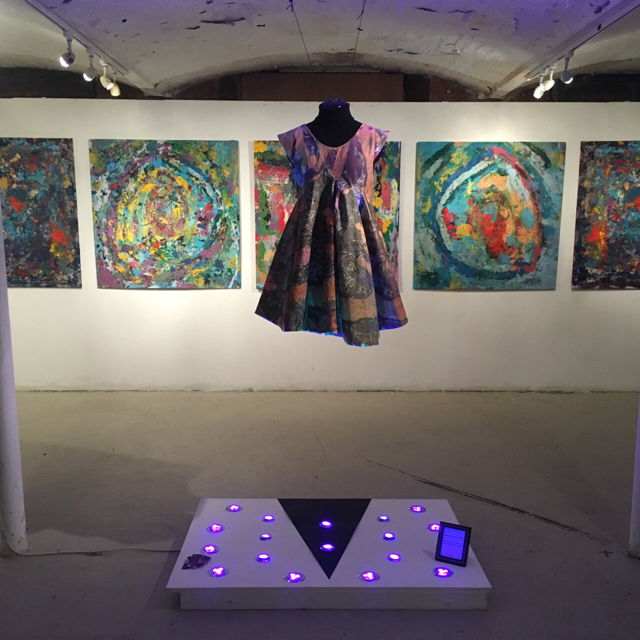 Sally Gilford's dress hanging in front of the five paintings at the centre of the exhibition