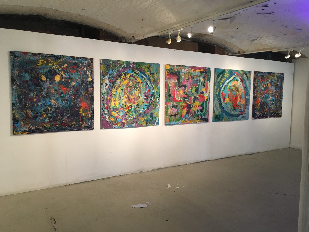 Angled view of the five paintings hung along the gallery wall