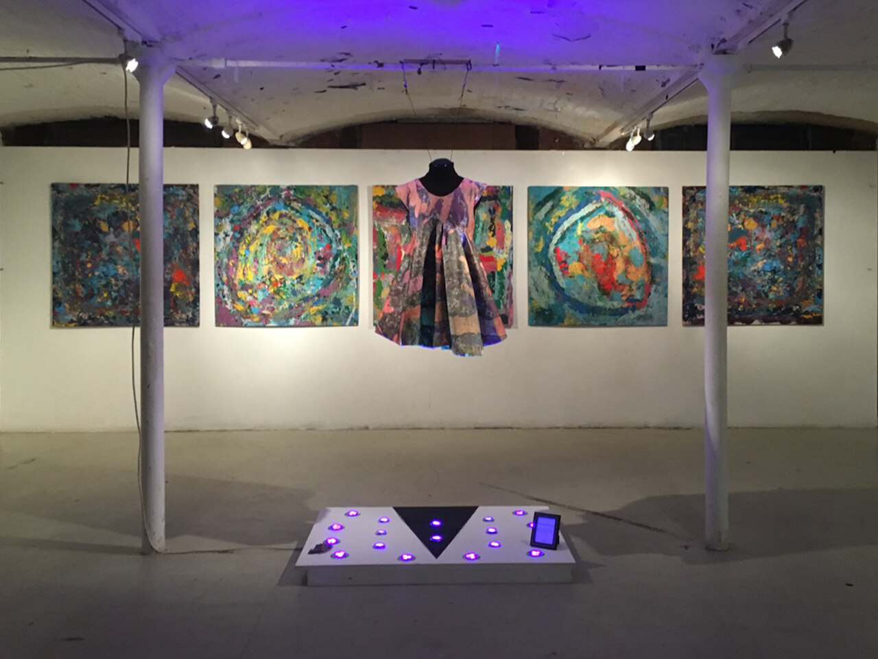 Wide view of the full installation, the dress hanging among the five paintings