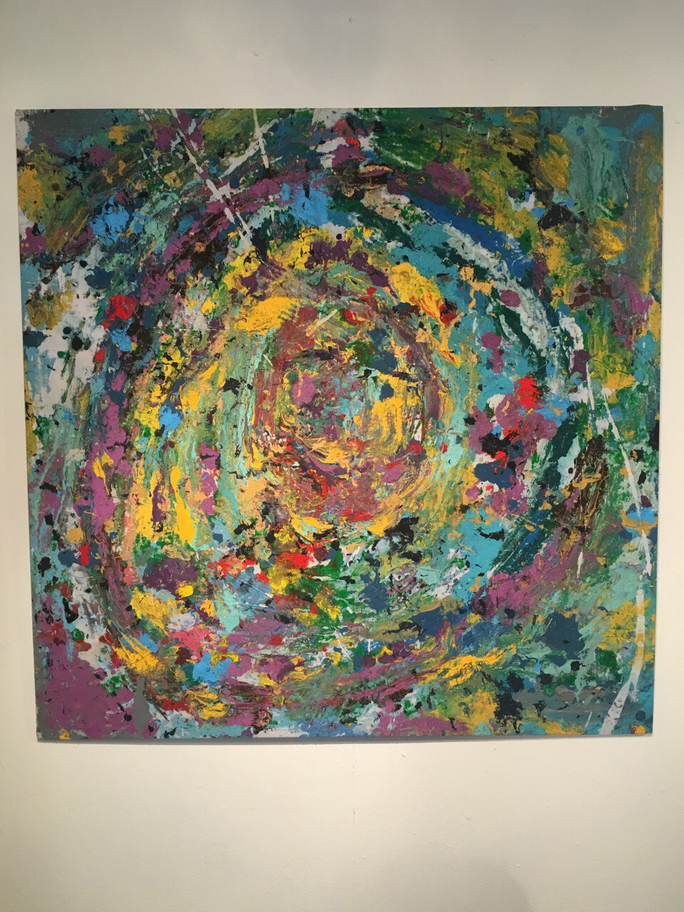 Close view of one of the paintings, a spiralling circular composition in yellow, teal and pink