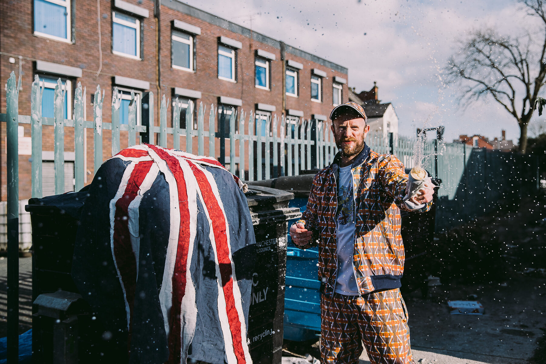 A fabric Union Jack draped over a bin, with Mark Jermyn in the patterned tracksuit reacting to a splash of drink, part of the Brexit photo series
