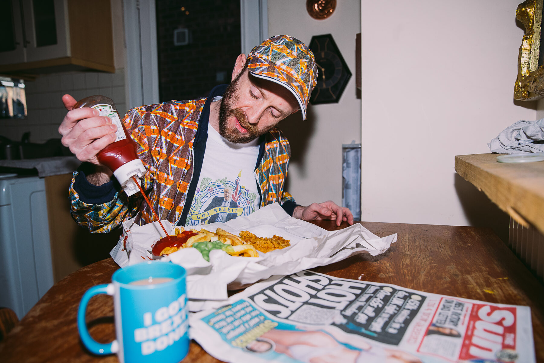 A staged kitchen table scene with a chip shop dinner, a mug reading 'I got Brexit done' and a copy of The Sun, part of the Brexit photo series