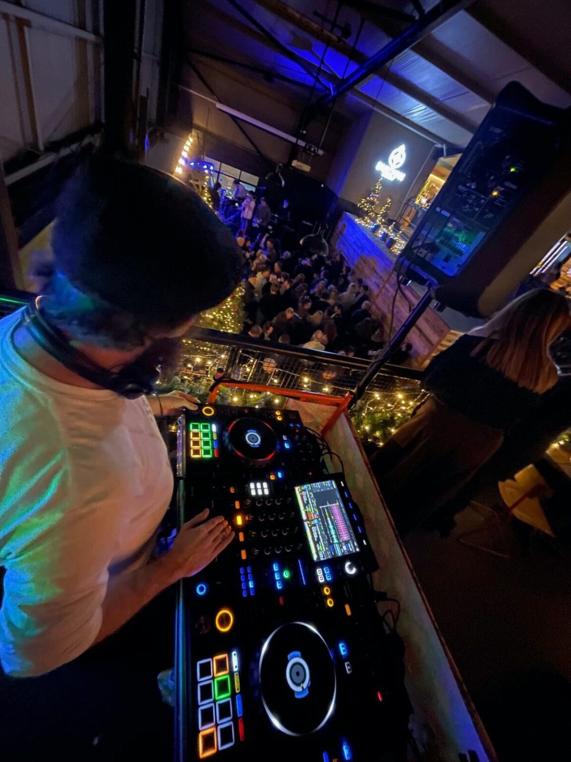 Looking over a DJ's shoulder at the controller and out towards a crowd in a dark room