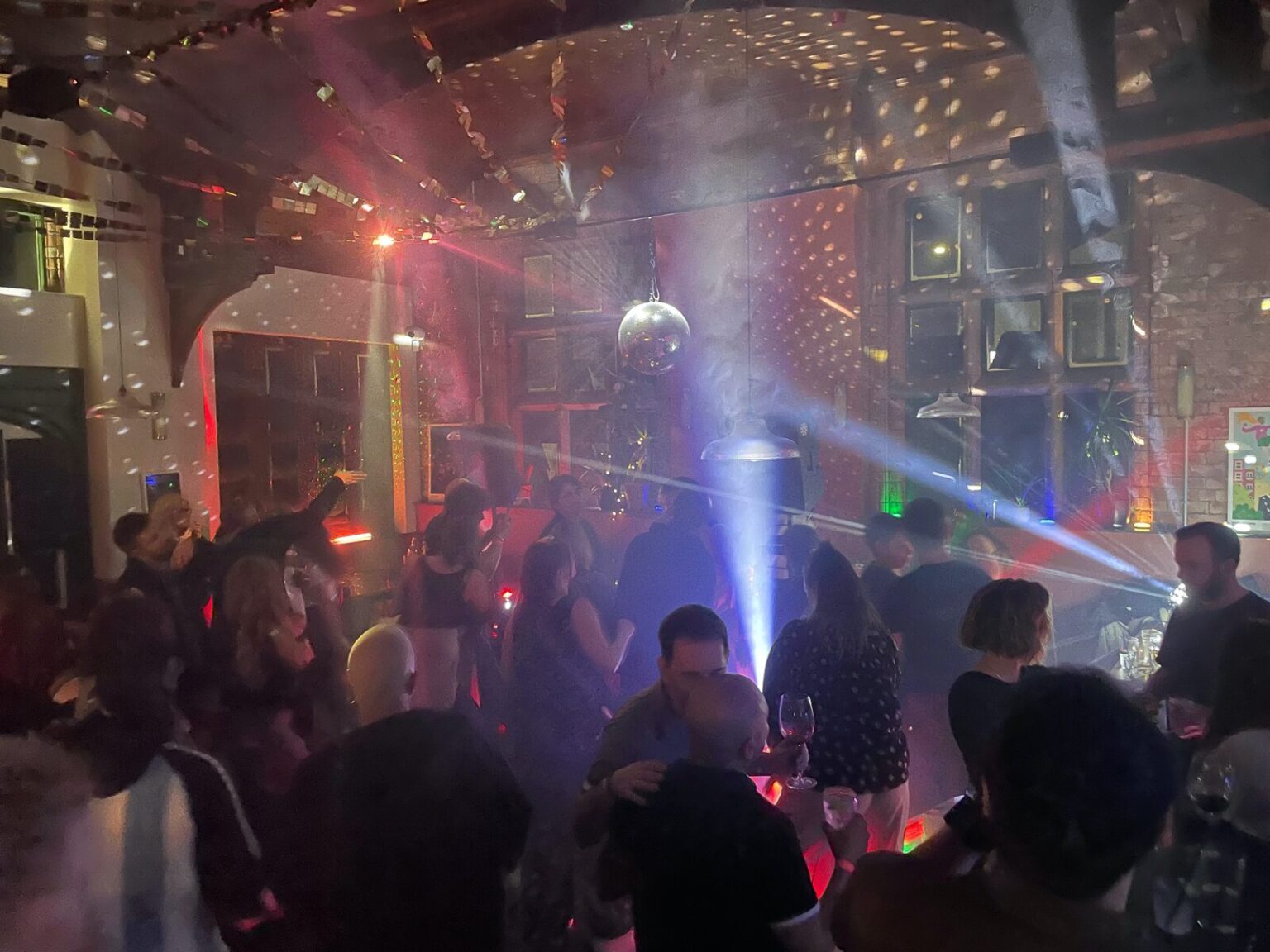 People dancing under a mirror ball with blue and pink beams cutting through the haze