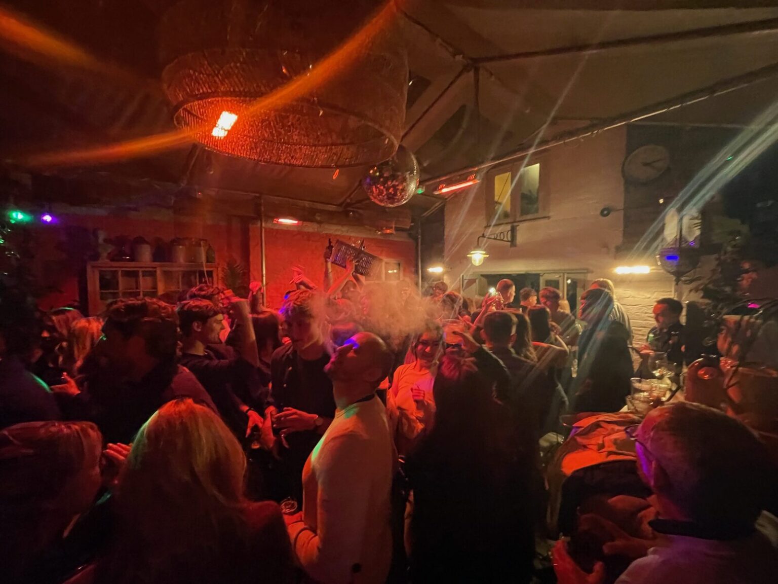 A packed room of people at a party under warm light, with a mirror ball above