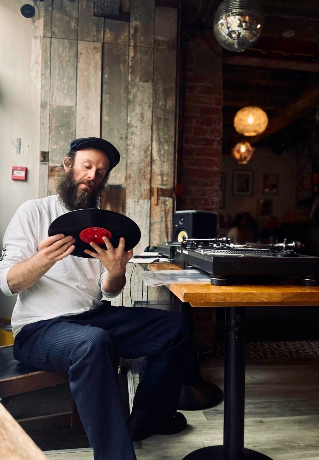 A person sitting with a record in their hands beside a pair of turntables, under a mirror ball