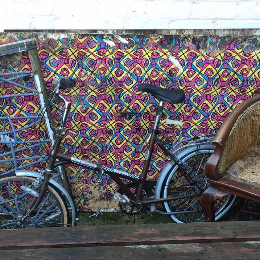 A bicycle leaning against a wall papered in the pattern in a public street