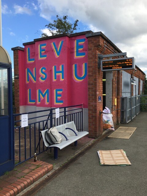 The Levenshulme Station Mural seen on the platform building alongside a train departure board