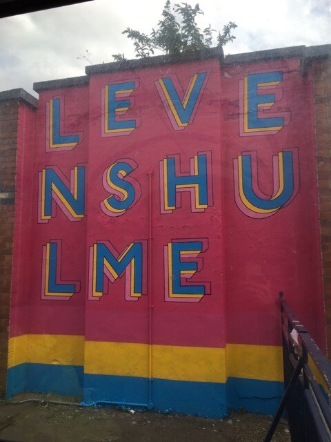 The finished Levenshulme Station Mural spelling out the station name in pink, blue and yellow across the platform building