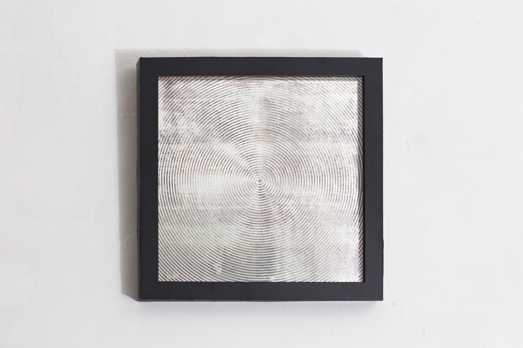 A framed mirror with a laser-etched and chemically eroded concentric ring pattern
