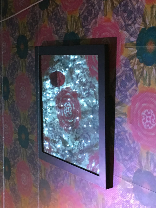 A framed mirror reflecting the lit Christmas tree, mounted on the custom floral wallpaper