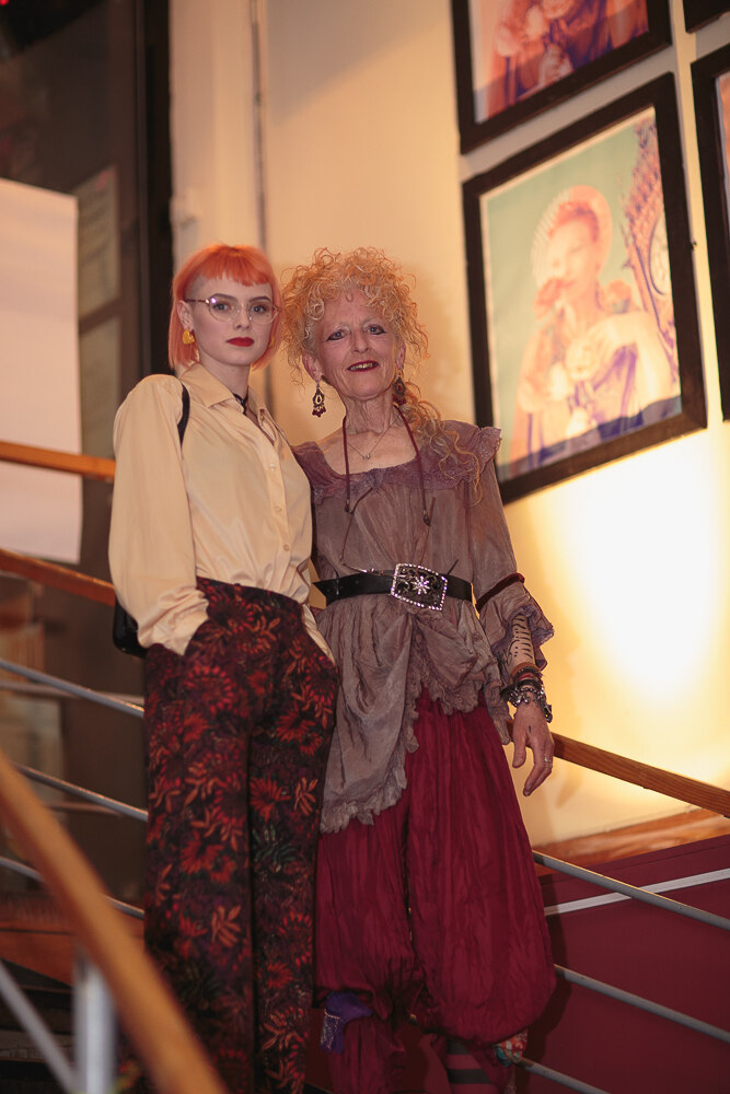 Costume competition entrants in tartan and vintage dress beside the exhibition wall