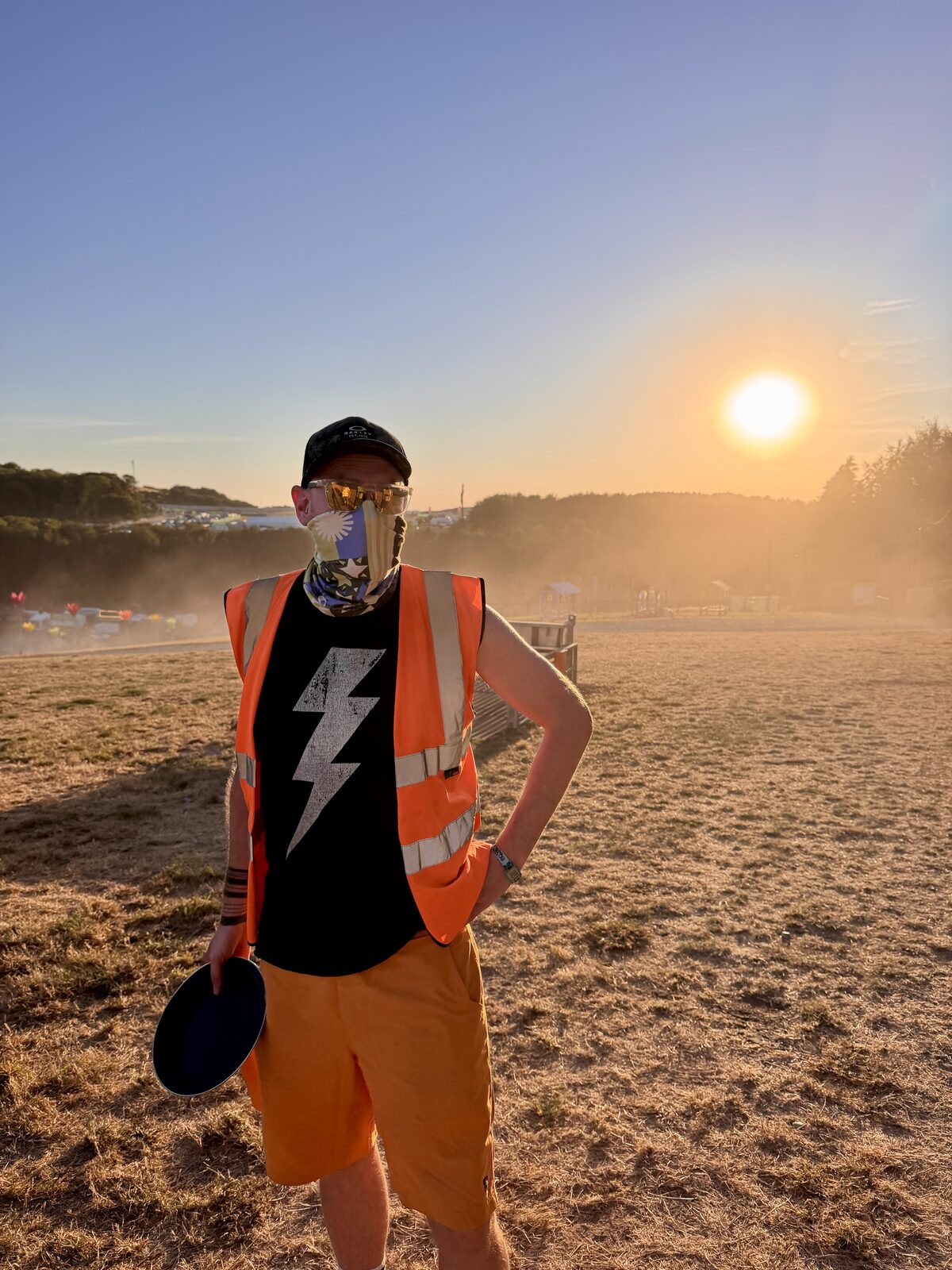 Standing on dry, dusty ground at Boomtown in a hi-vis vest and a dust mask, with the sun low through the haze
