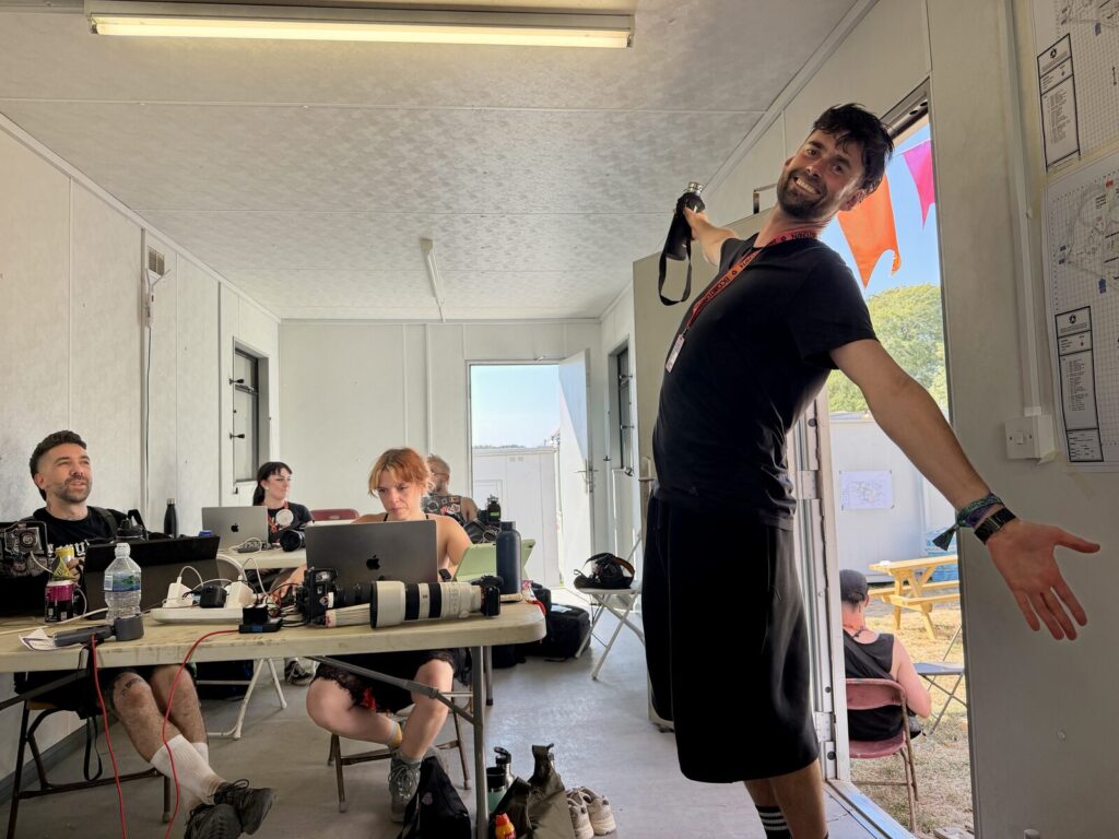 Three of the photography team working at laptops in the production office, one of them standing with a camera round his neck